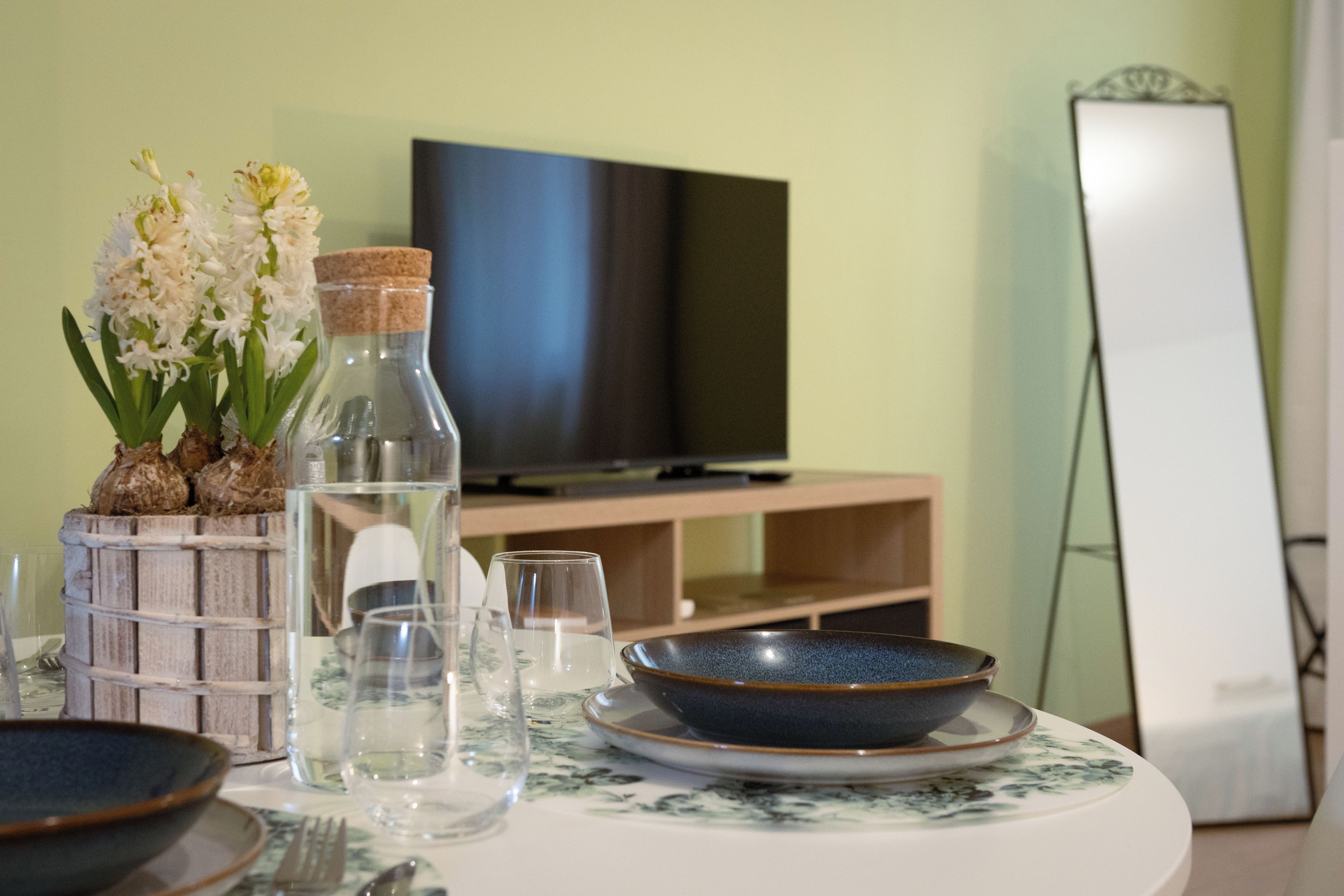 A dining area with a table set for two, a television, and a mirror.