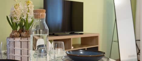 Un'area pranzo con un tavolo apparecchiato per due persone, una televisione e uno specchio.