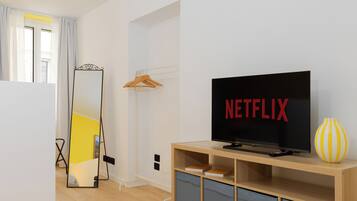 Un soggiorno moderno con una TV a schermo piatto che mostra il logo di Netflix, un mobile TV in legno, uno specchio e un vaso giallo.