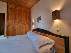 Un dormitorio con cabecera de madera, cama con ropa de cama blanca, lámpara de pared y paneles de madera en las paredes.