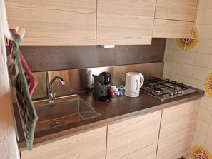 A kitchen with a stainless steel sink, a coffee maker, a kettle, and a gas stove. - Zoncolan Secret Escape - Wifi - Netflix - Parking (Ravascletto)