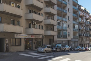 A multi-story residential building with balconies, a storefront with signage, and parked cars along the street. - Trieste Zona Burlo - Wi-fi, Terrazzo, Ascensore (Trieste)