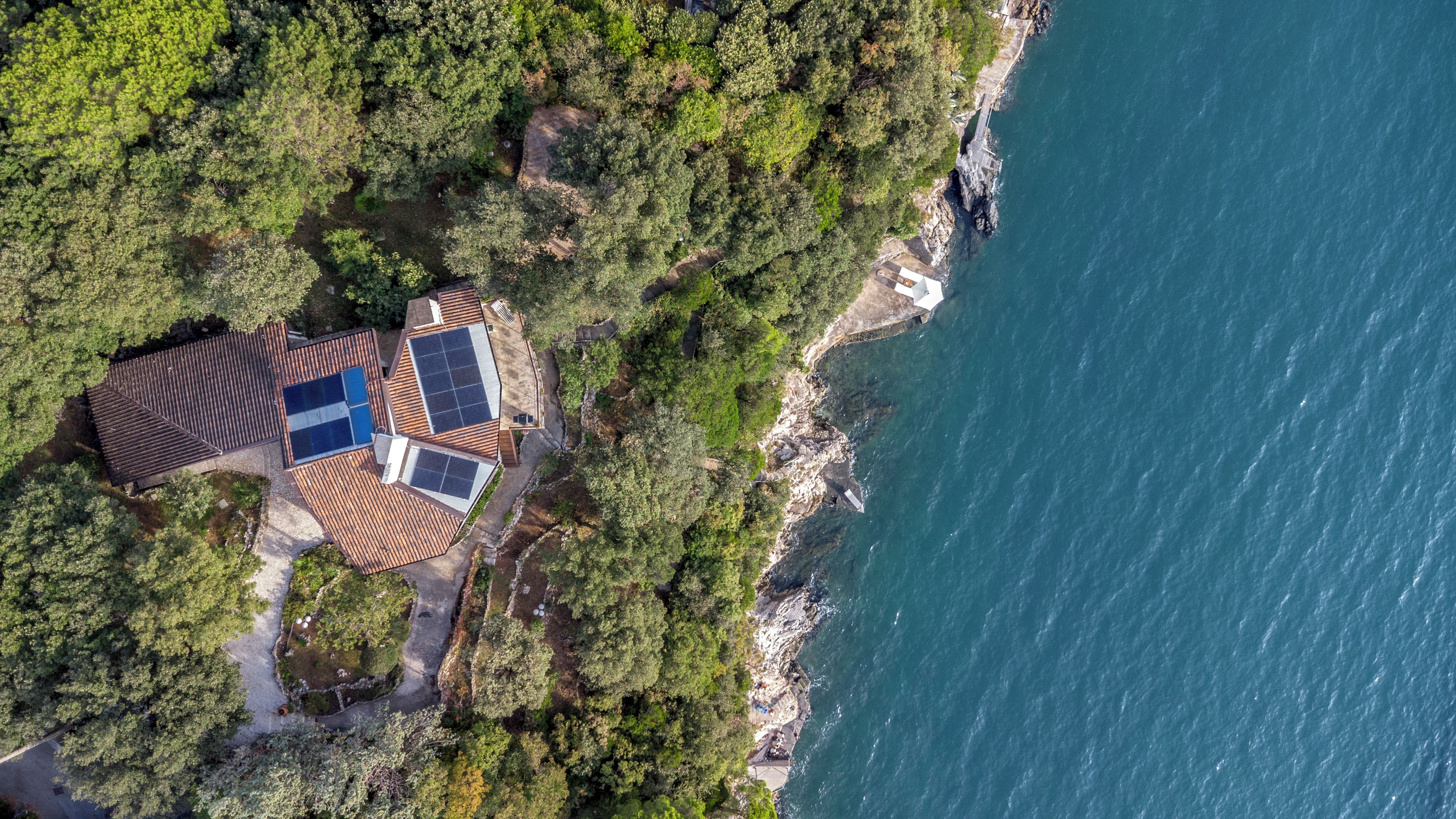 A coastal property with a large roof area, a swimming pool, and a rocky shoreline.