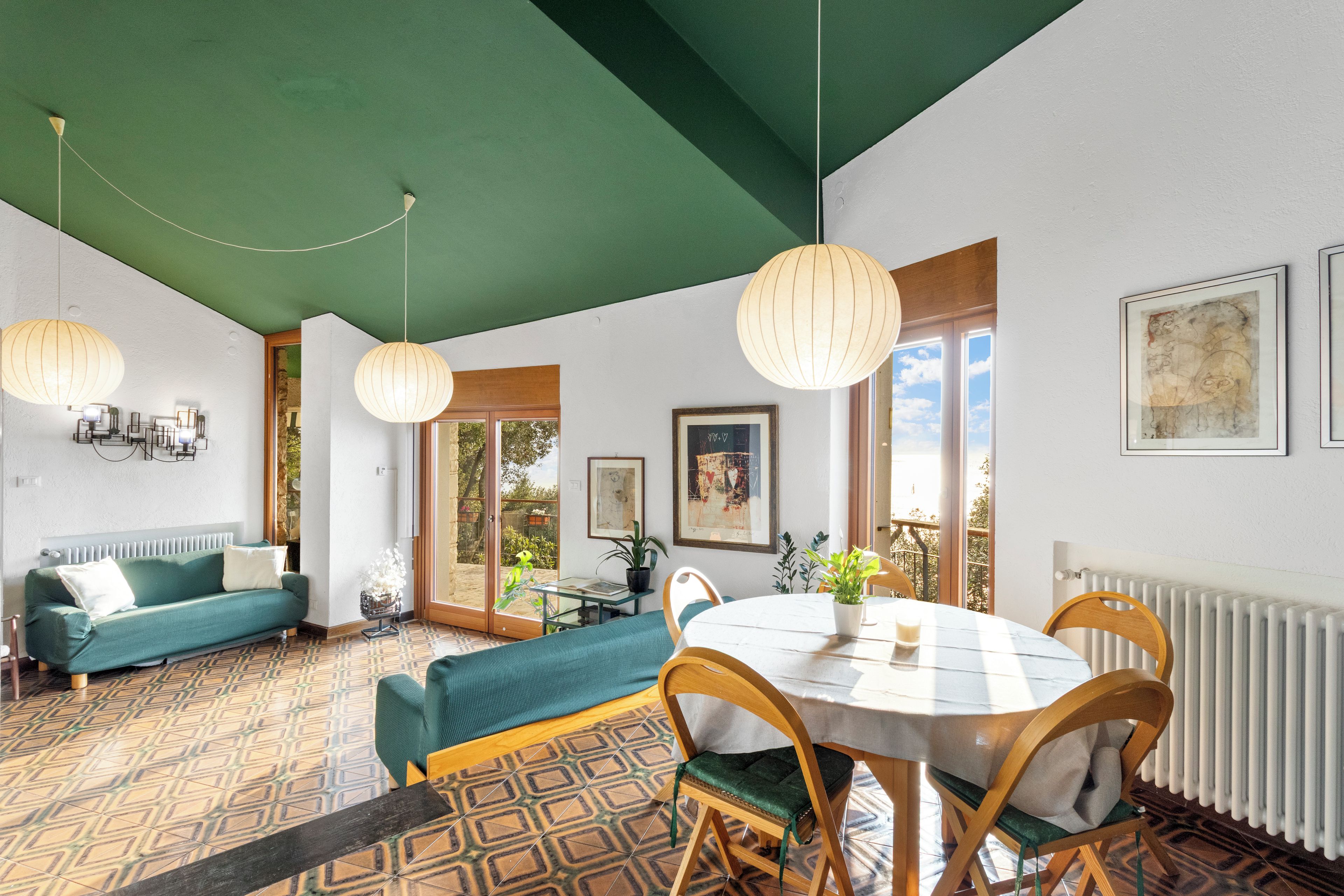 Une pièce avec un plafond vert, un canapé, une table à manger avec des chaises et une vue sur l’extérieur, visible à travers une porte vitrée.
