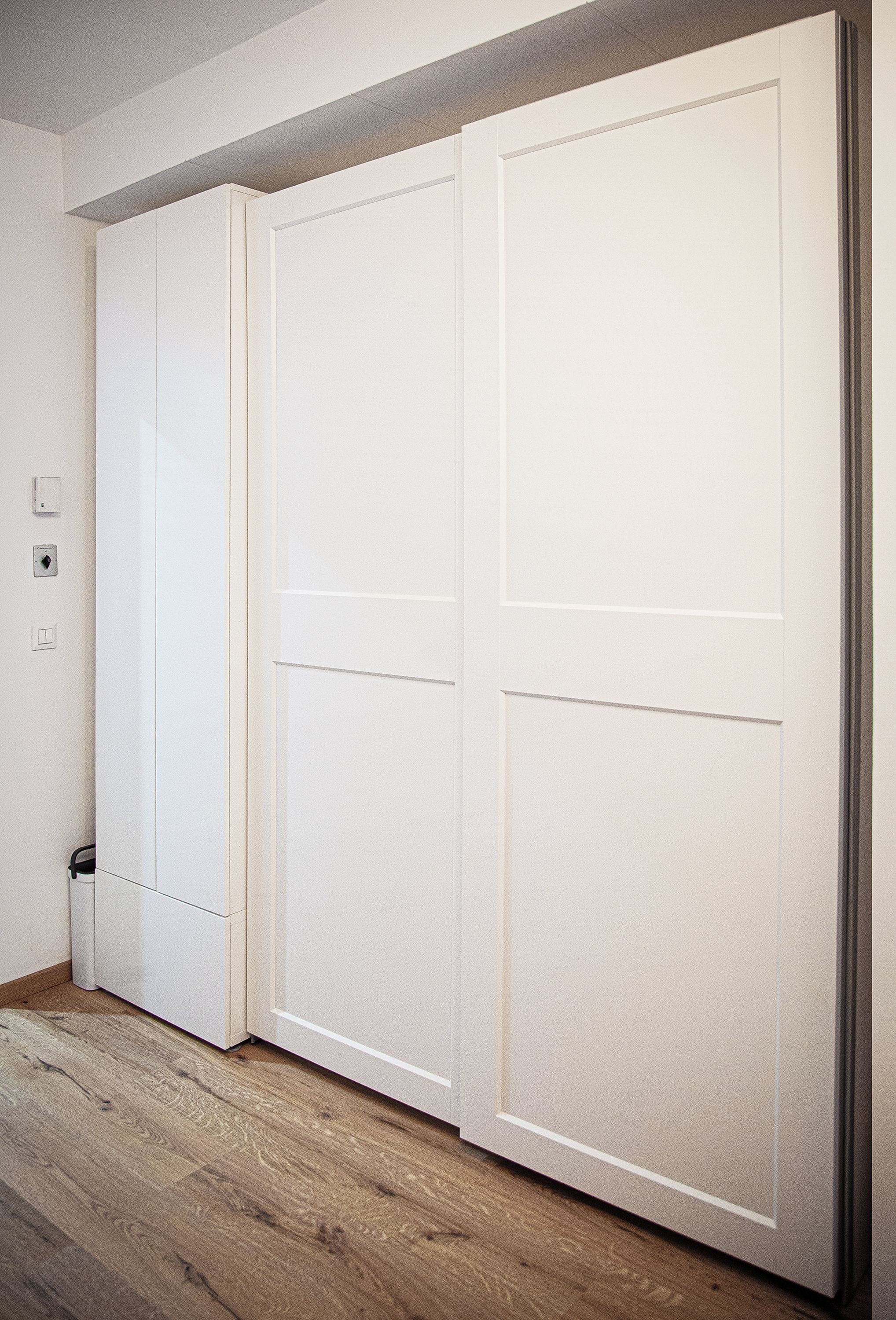 A room with a wooden floor, a white door, and a light switch on the wall.