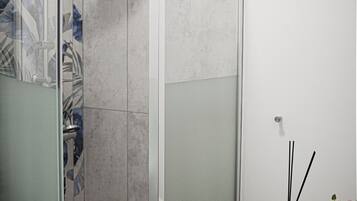 A modern bathroom with a glass-enclosed shower, a small vanity with a bottle of perfume, and a towel on the floor.