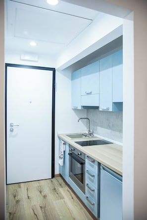 Una cuina compacta amb forn integrat, un rentapeus i armaris de color blau clar.