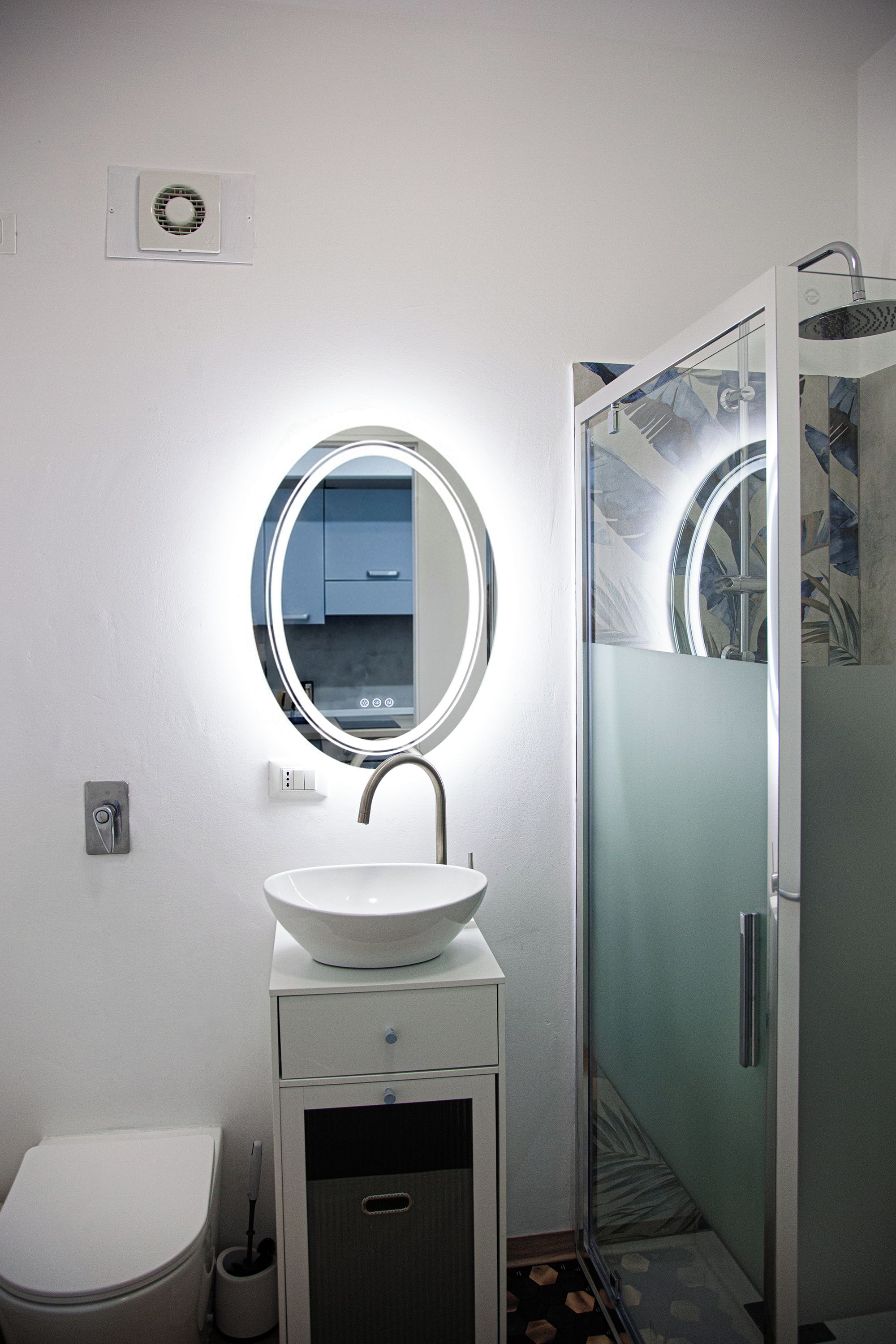 A bathroom with a round mirror, a white sink, a toilet, and a shower enclosure.