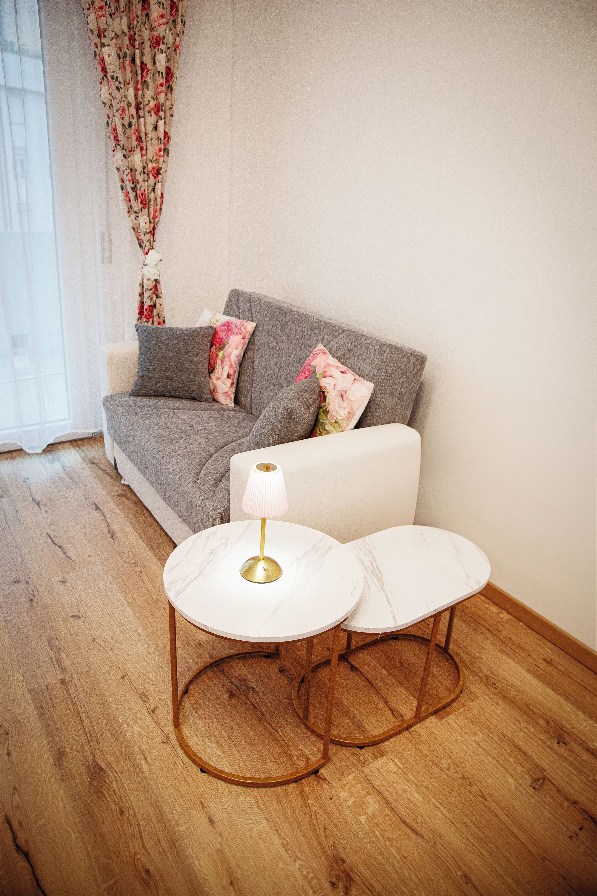 Ein modernes Wohnzimmer mit einem grauen Sofa, zwei weißen Marmortischen und einer Goldlampe.