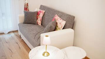 Ein modernes Wohnzimmer mit einem grauen Sofa, zwei weißen Marmortischen und einer Goldlampe.