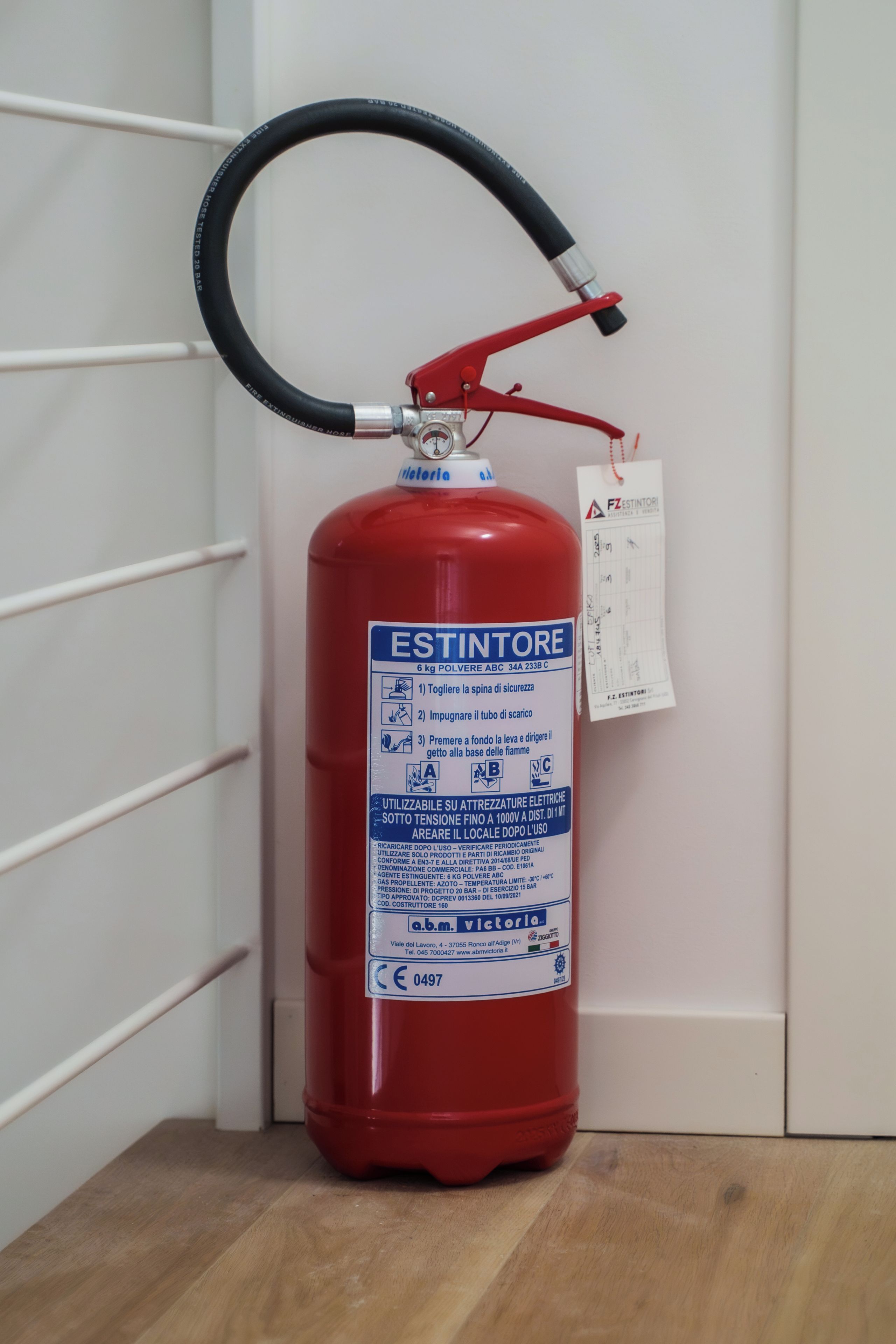 Un extintor rojo sujeto a una pared blanca con un soporte de metal.