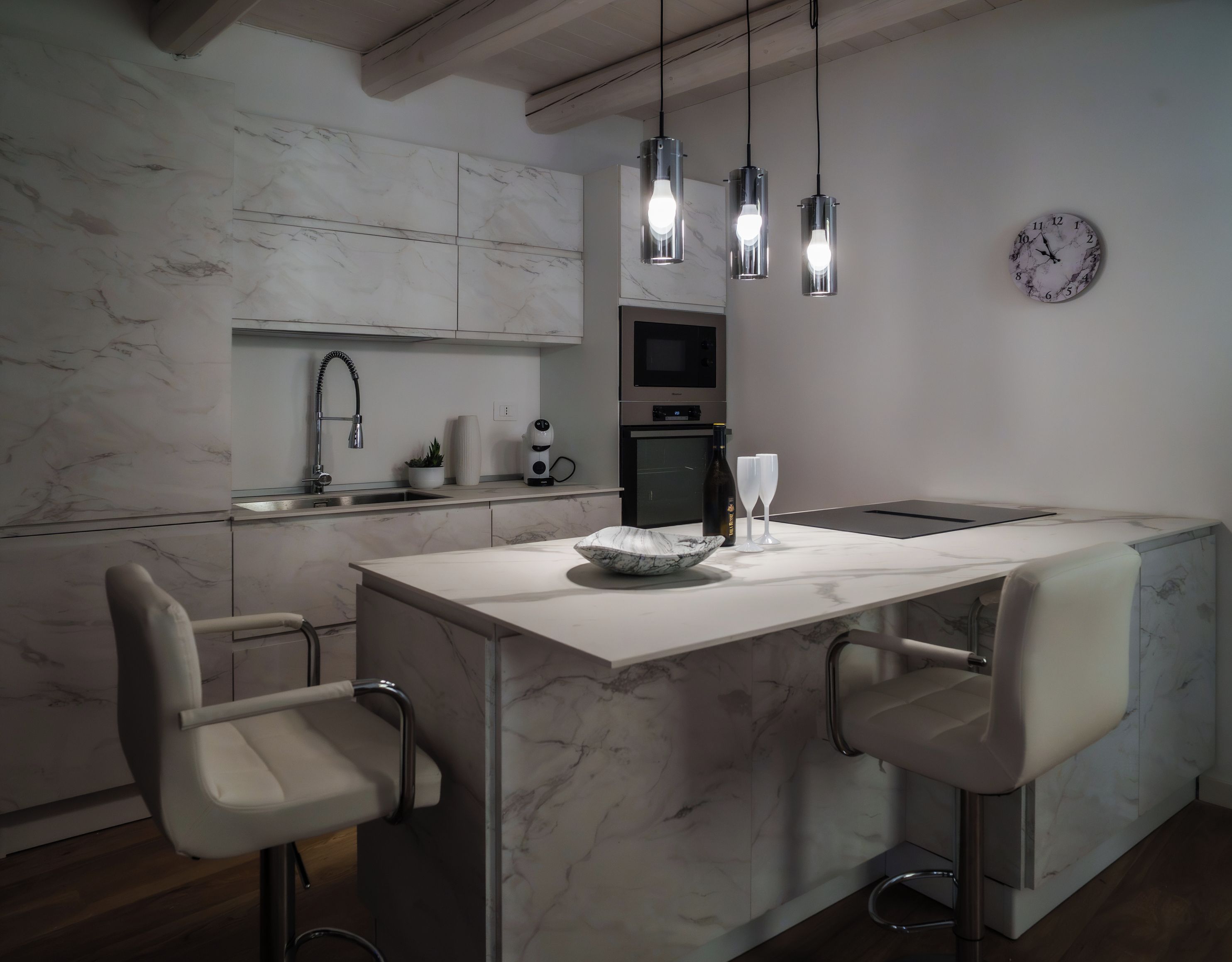 Una cocina moderna con encimera de mármol, electrodomésticos de acero inoxidable, iluminación colgante y horno empotrado.