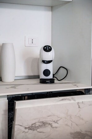 Um purificador de ar branco sobre uma bancada de mármore, com uma tomada e um vaso branco ao fundo.