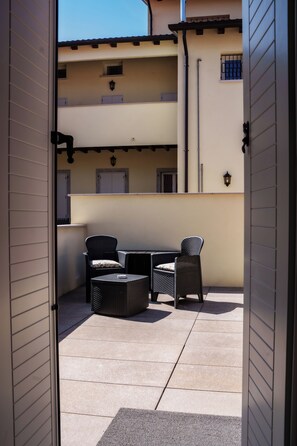 An outdoor patio area with a table and two chairs, a small round table, and a wall-mounted light fixture.