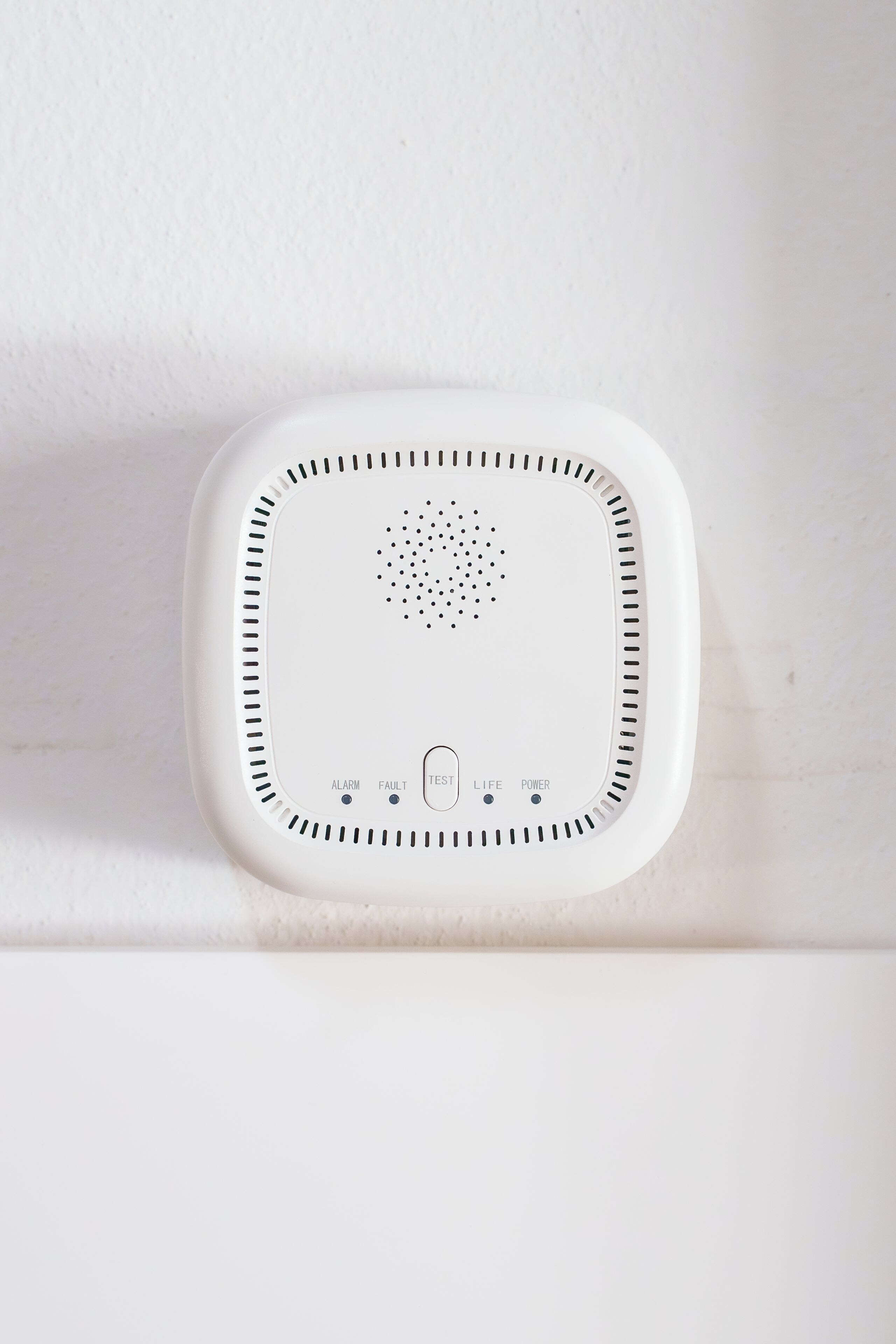 Dispositivo bianco e squadrato con una griglia di fori nella parte superiore e quattro pulsanti etichettati 'ALARM', 'FAULT', 'TEST', 'LIFE' e 'POWER' nella parte inferiore.