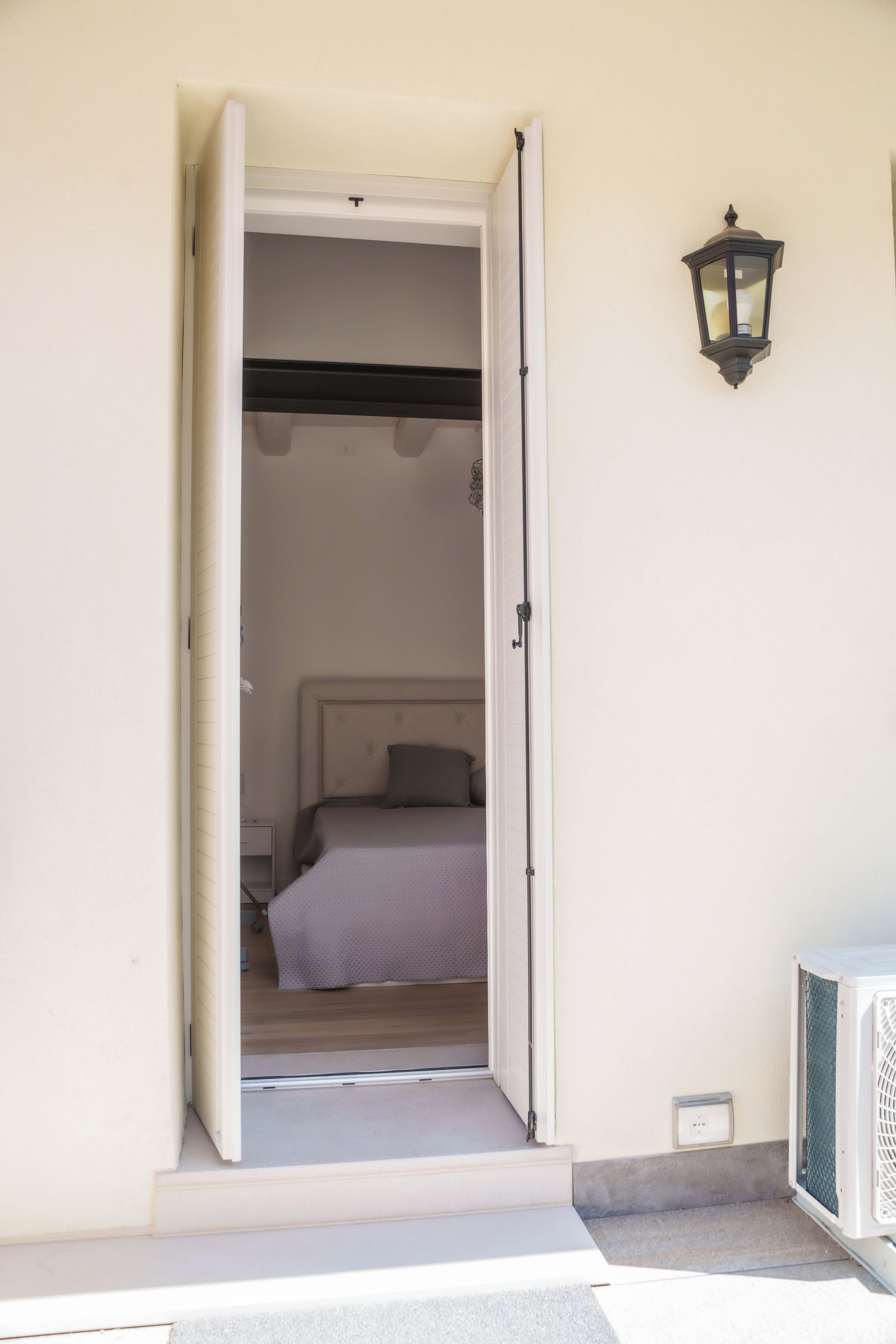 Un umbral abierto que da a un dormitorio con una cama, una mesita de noche y una lámpara de pared.