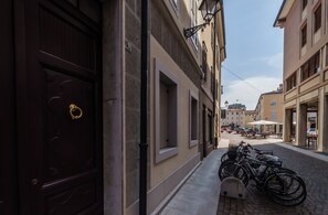 A narrow street with buildings on either side, a row of bicycles parked on the sidewalk, and a cobblestone road.