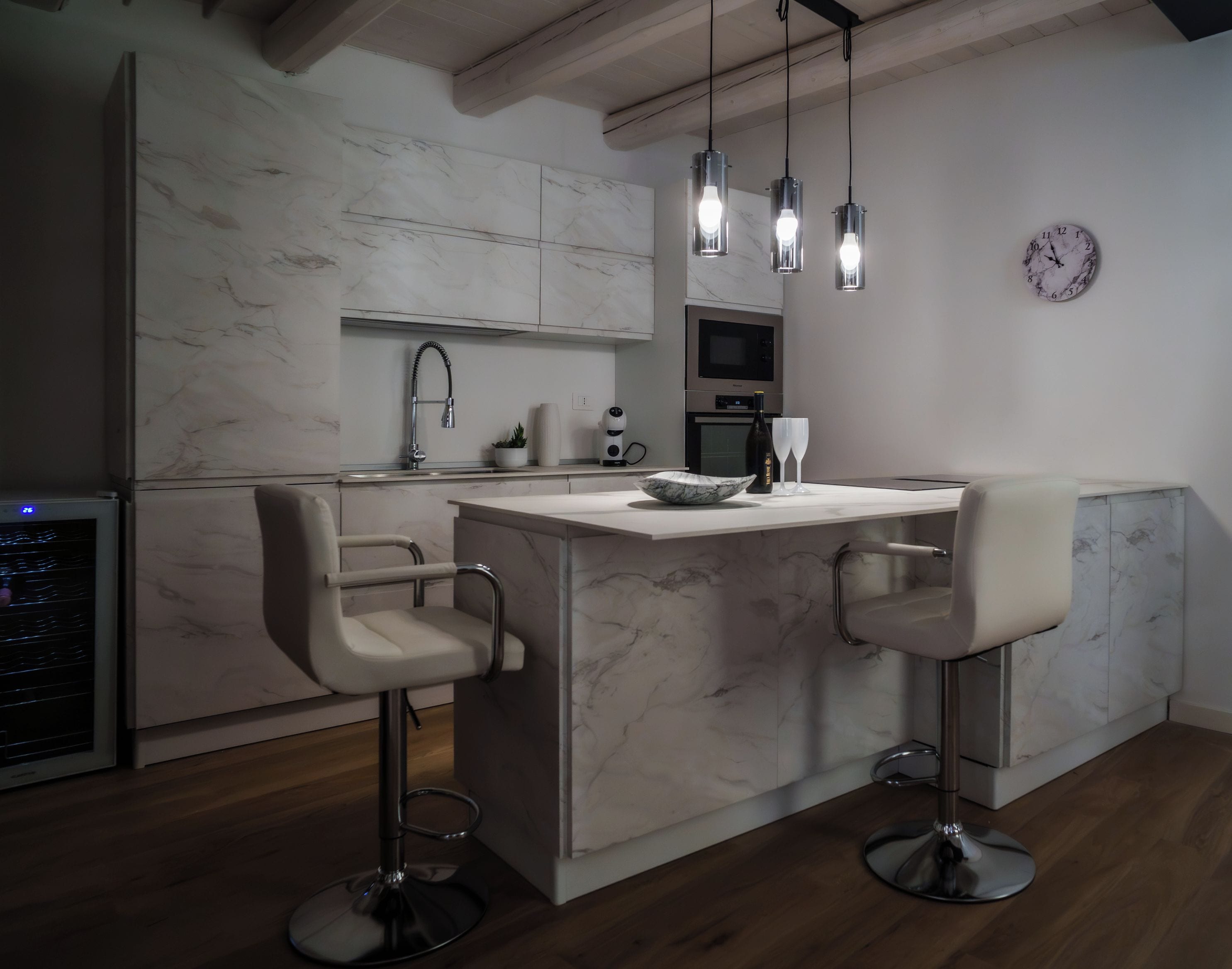 Une cuisine moderne avec des plans de travail en marbre, un four encastré, un four à micro-ondes et une horloge murale.