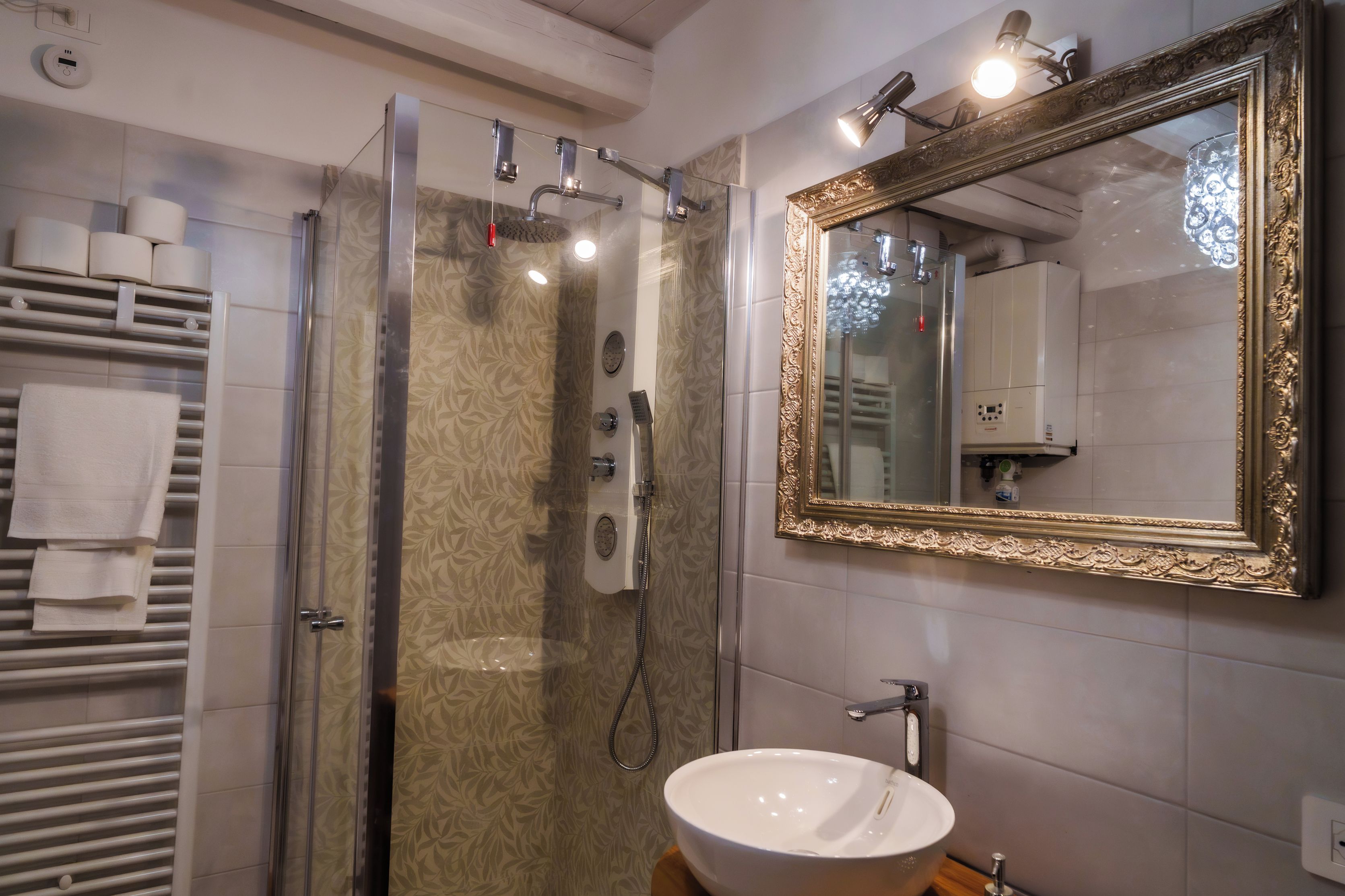 Un bagno con cabina doccia in vetro, un lavandino bianco e uno specchio grande con cornice decorata.
