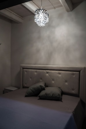 A bedroom with a tufted headboard, two pillows, a small bedside table, and a hanging light fixture. - Urban Wine Studio Apartment con Terrazzo (Gorizia)