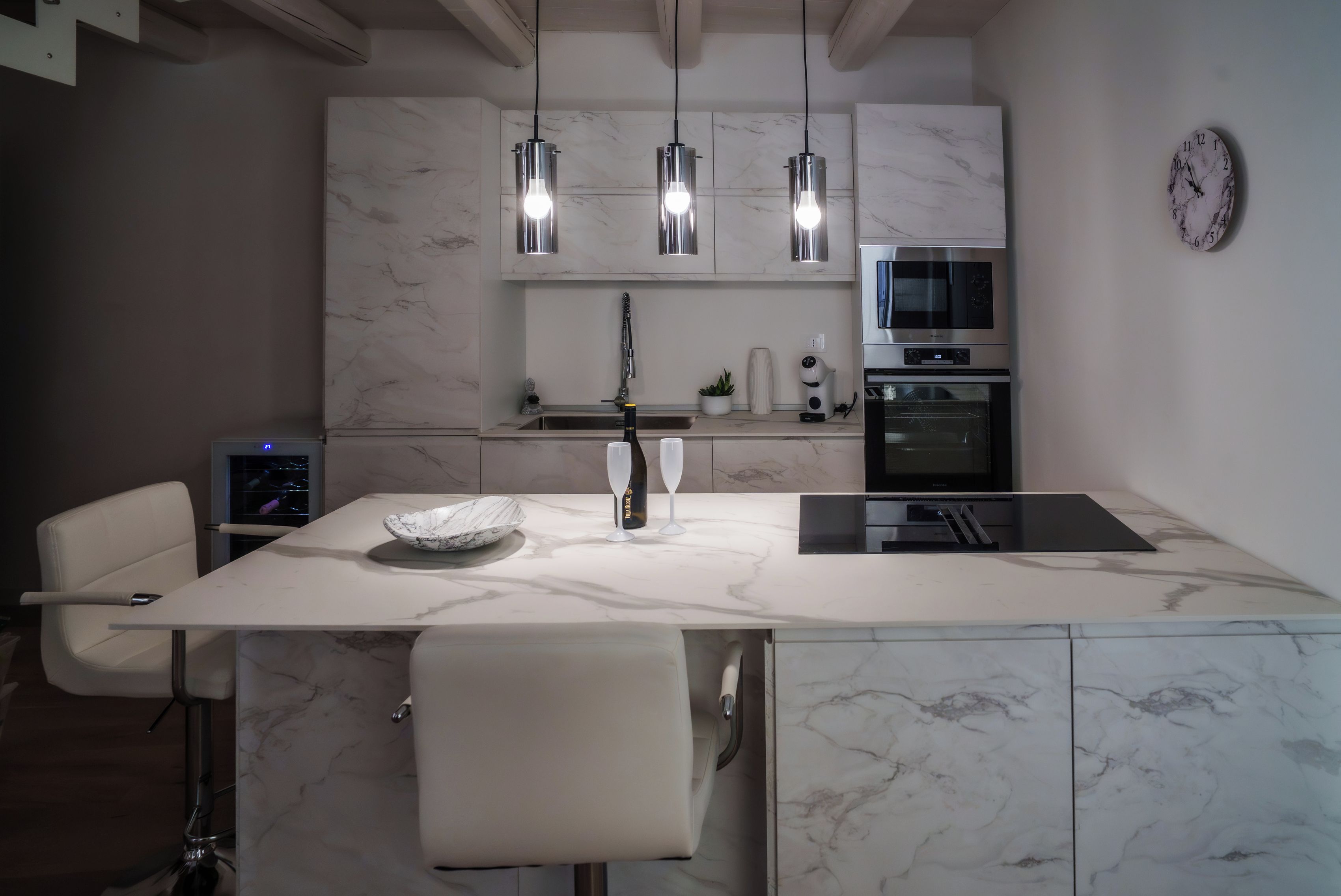 A modern kitchen with a marble countertop, a built-in oven, a sink, and pendant lighting.