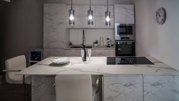 A modern kitchen with a marble countertop, a built-in oven, a sink, and pendant lighting.