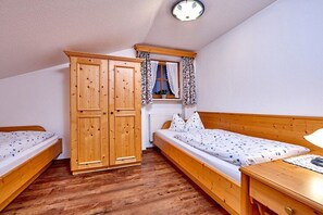 Een slaapkamer met twee houten bedden, een houten kledingkast en een raam met gordijnen.