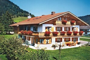 A two-story chalet with a balcony, surrounded by greenery and hills. - 4 "Guesthouse Anneliese" (Wallgau)