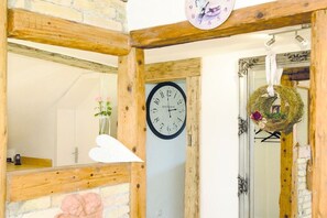 A rustic interior with exposed wooden beams, a wall clock, and a mirror reflecting a room with a bed and a vase with flowers. - Alpenflair holiday apartment Almfried 204 (Oberstdorf)