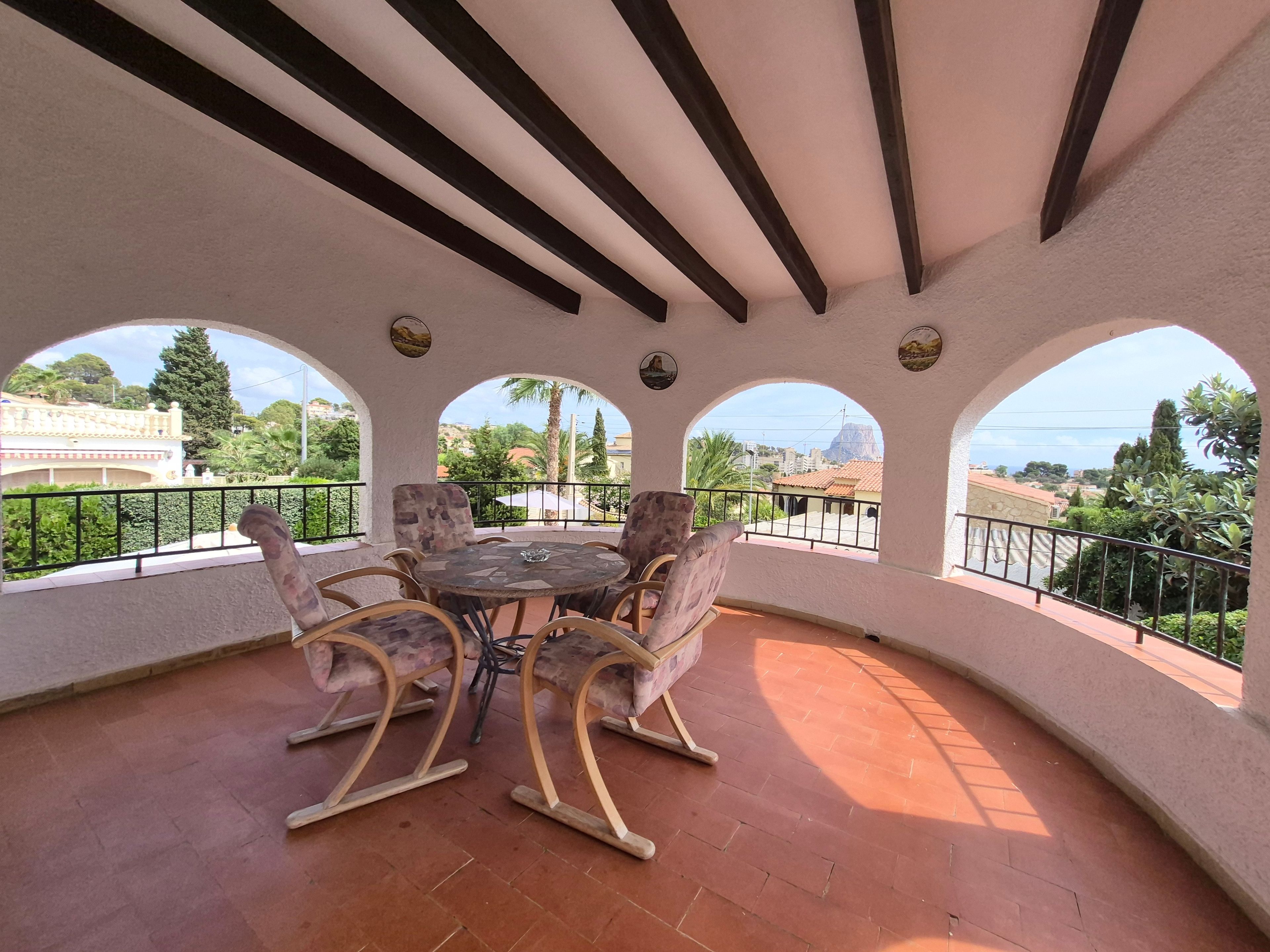 A covered patio with a round table and four chairs, a tiled floor, and a view of a town and hills.