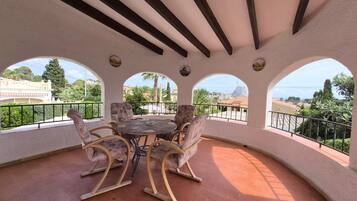 A covered patio with a round table and four chairs, a tiled floor, and a view of a town and hills.