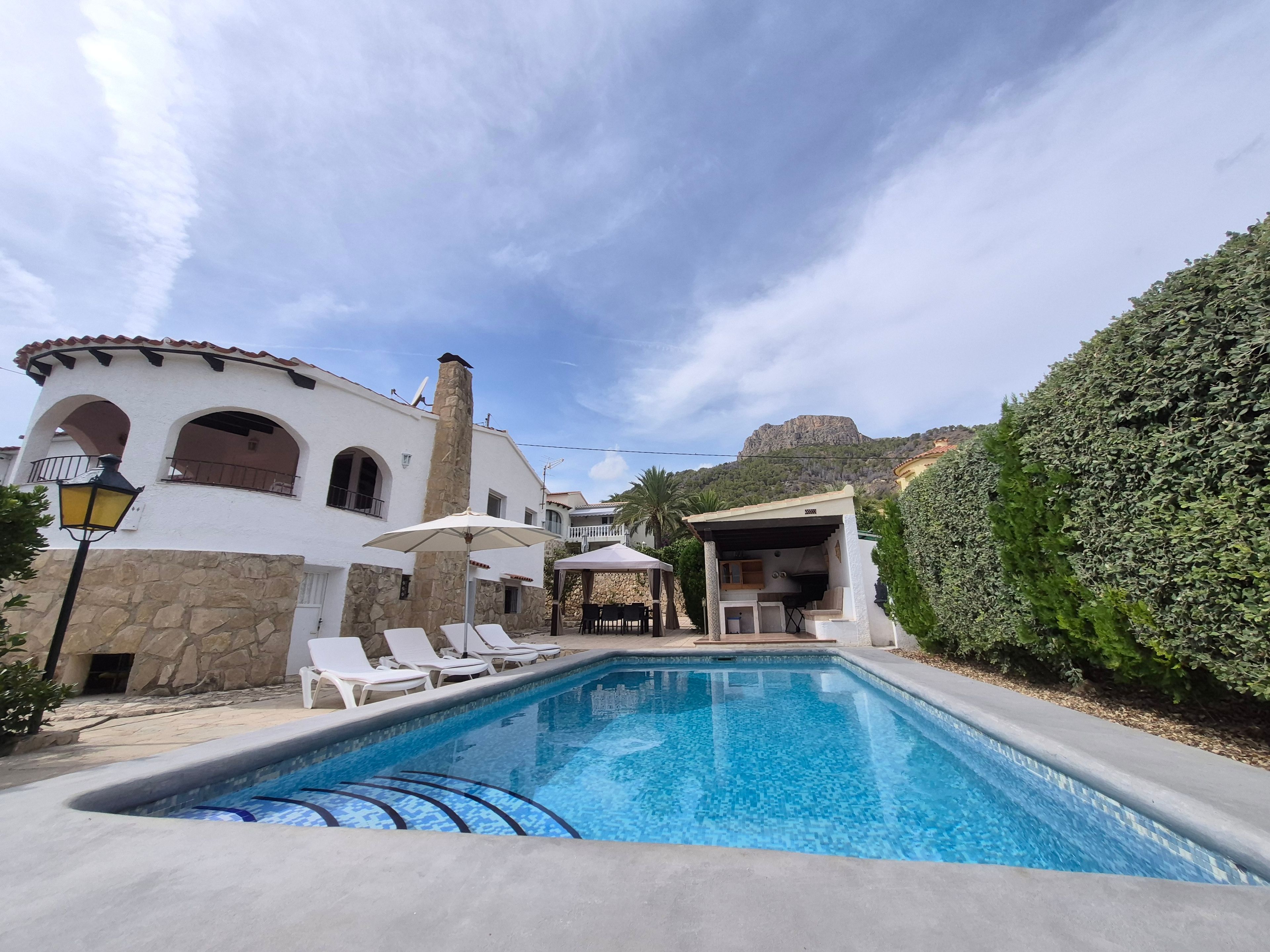 A swimming pool with lounge chairs, a stone building with arches, and a view of a mountain.