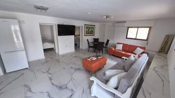 Een ruime woonkamer met een witte bank, een rode bank, een eettafel met stoelen, en een keuken met een koelkast.
