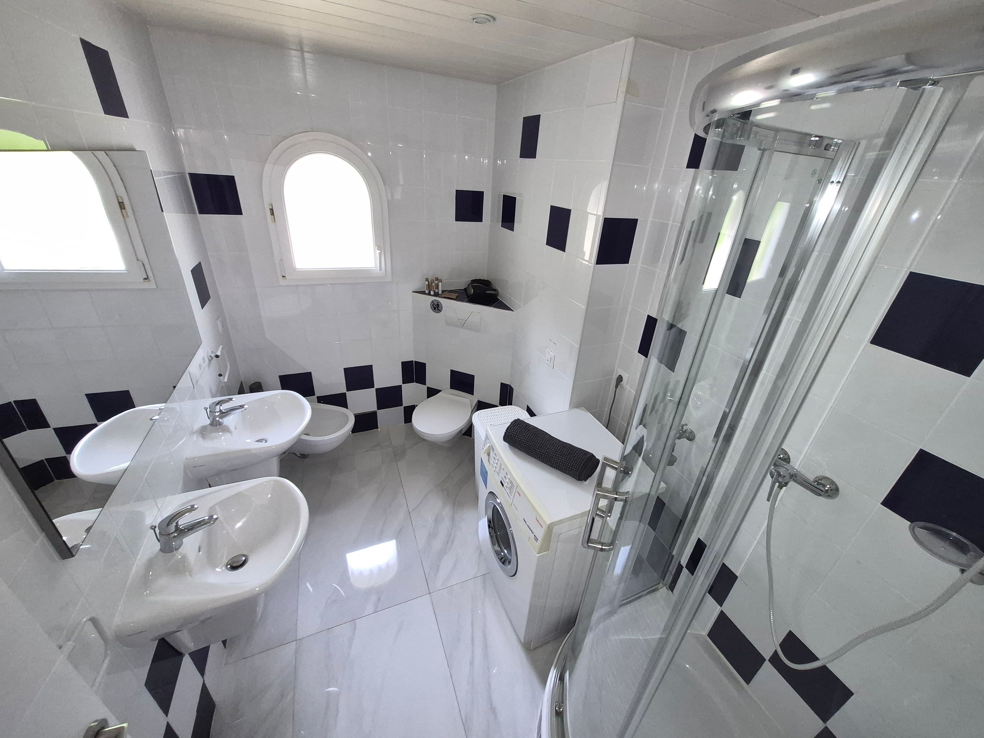 Ein Badezimmer mit Waschbecken, zwei Toiletten, einer Dusche und einem Fenster.