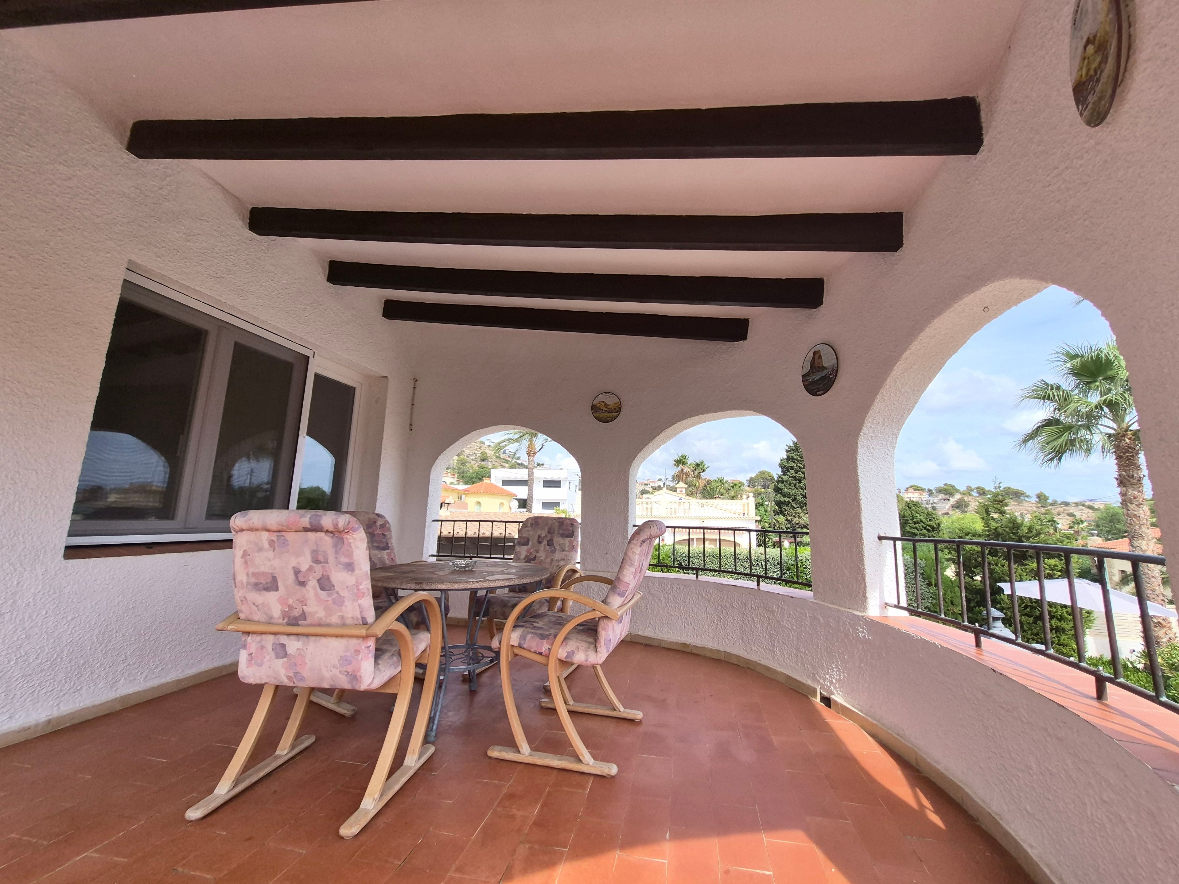 A covered patio area with a table and chairs, a window, and a view of the surrounding landscape.