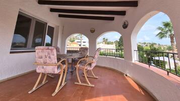 A covered patio area with a table and chairs, a window, and a view of the surrounding landscape.