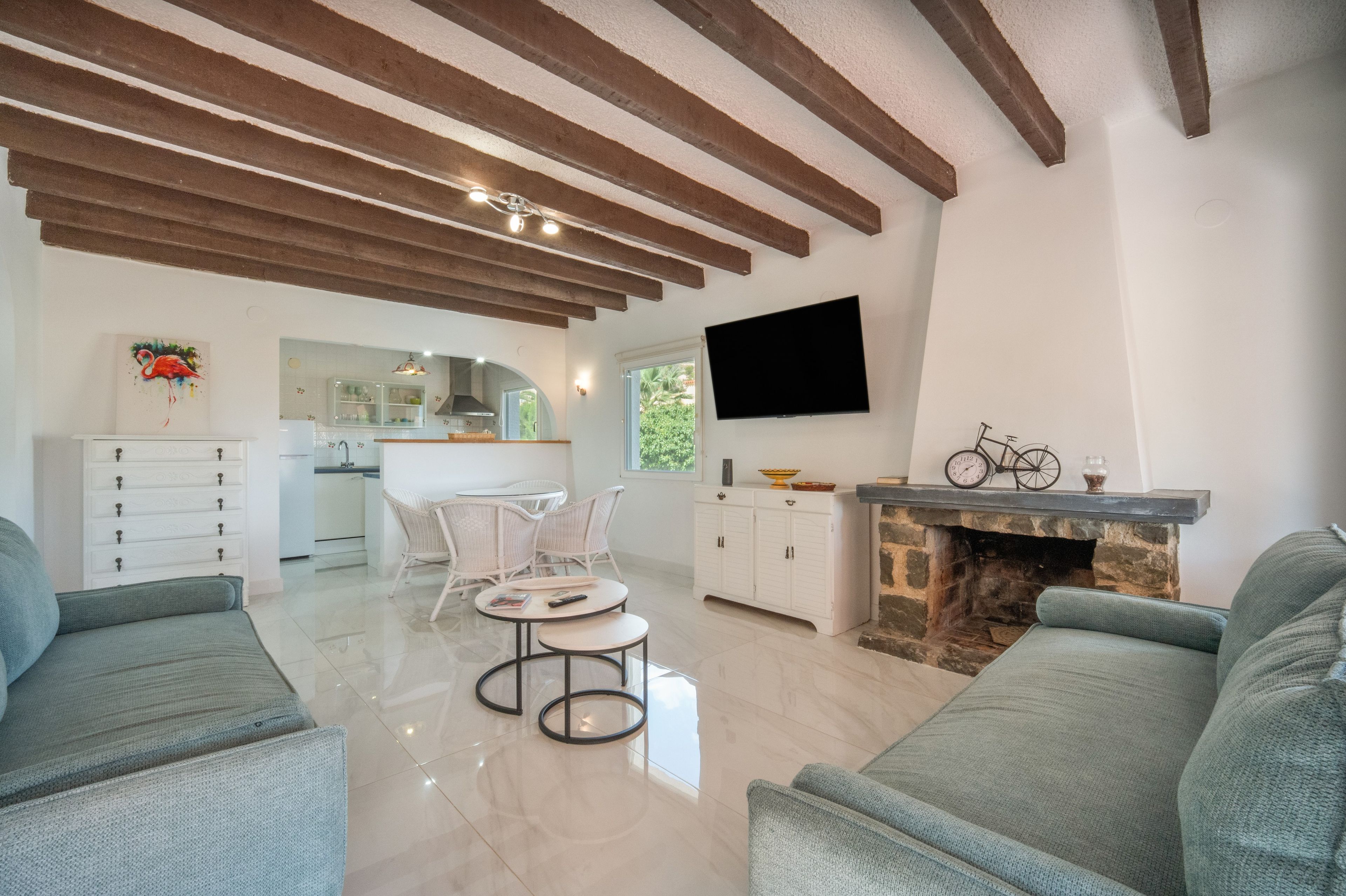 Una sala de estar moderna con chimenea, televisor y una cocina al fondo.