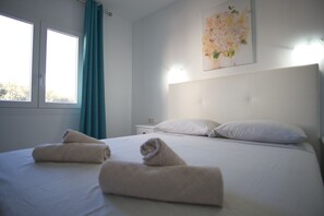 Ein Hotelzimmer mit einem Bett, zwei Kissen, einem Nachttisch, einem Wandbild und einem Fenster mit Vorhängen.