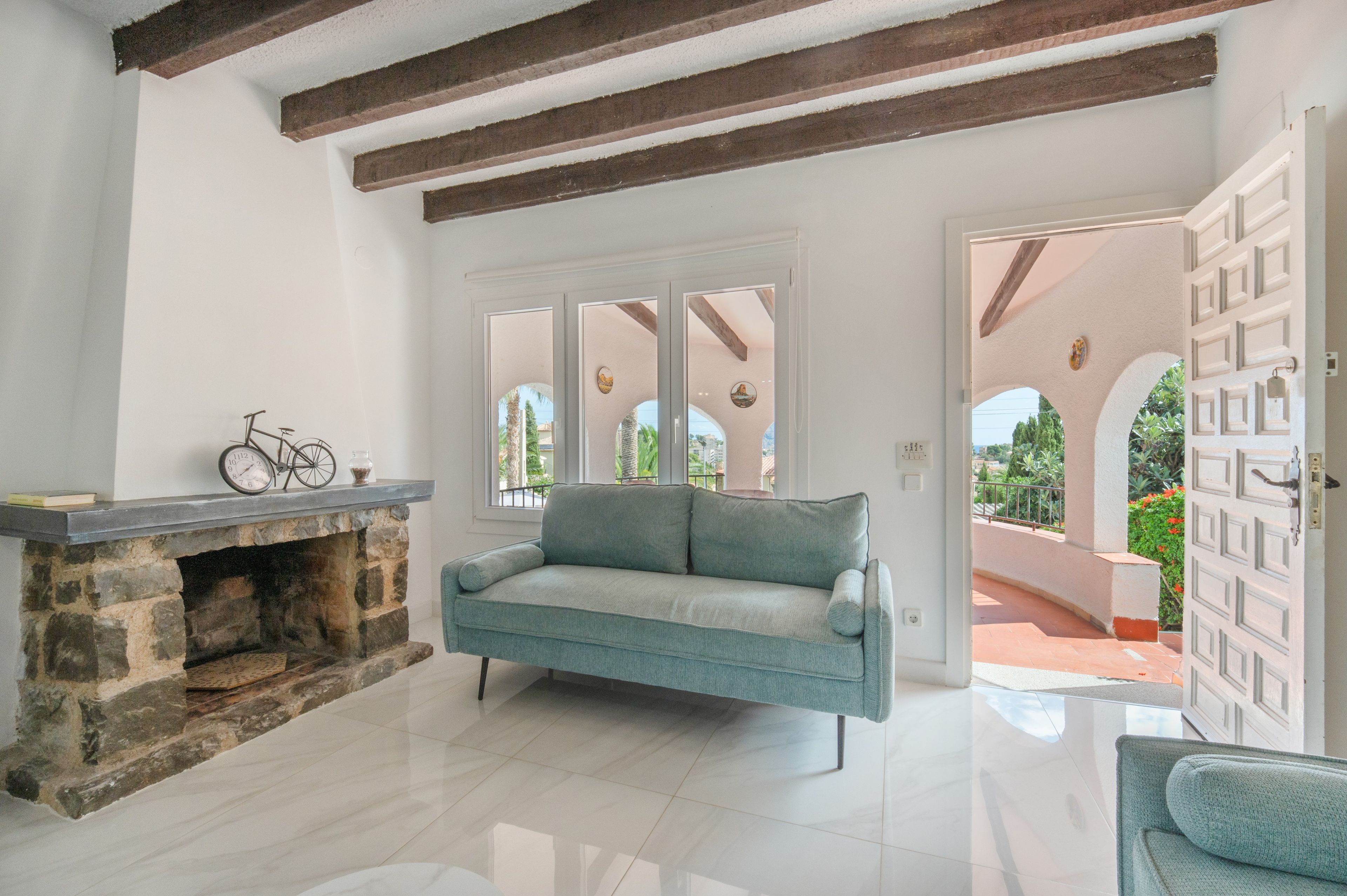 A room with a stone fireplace, a sofa, and a view through a glass door to an outdoor area.