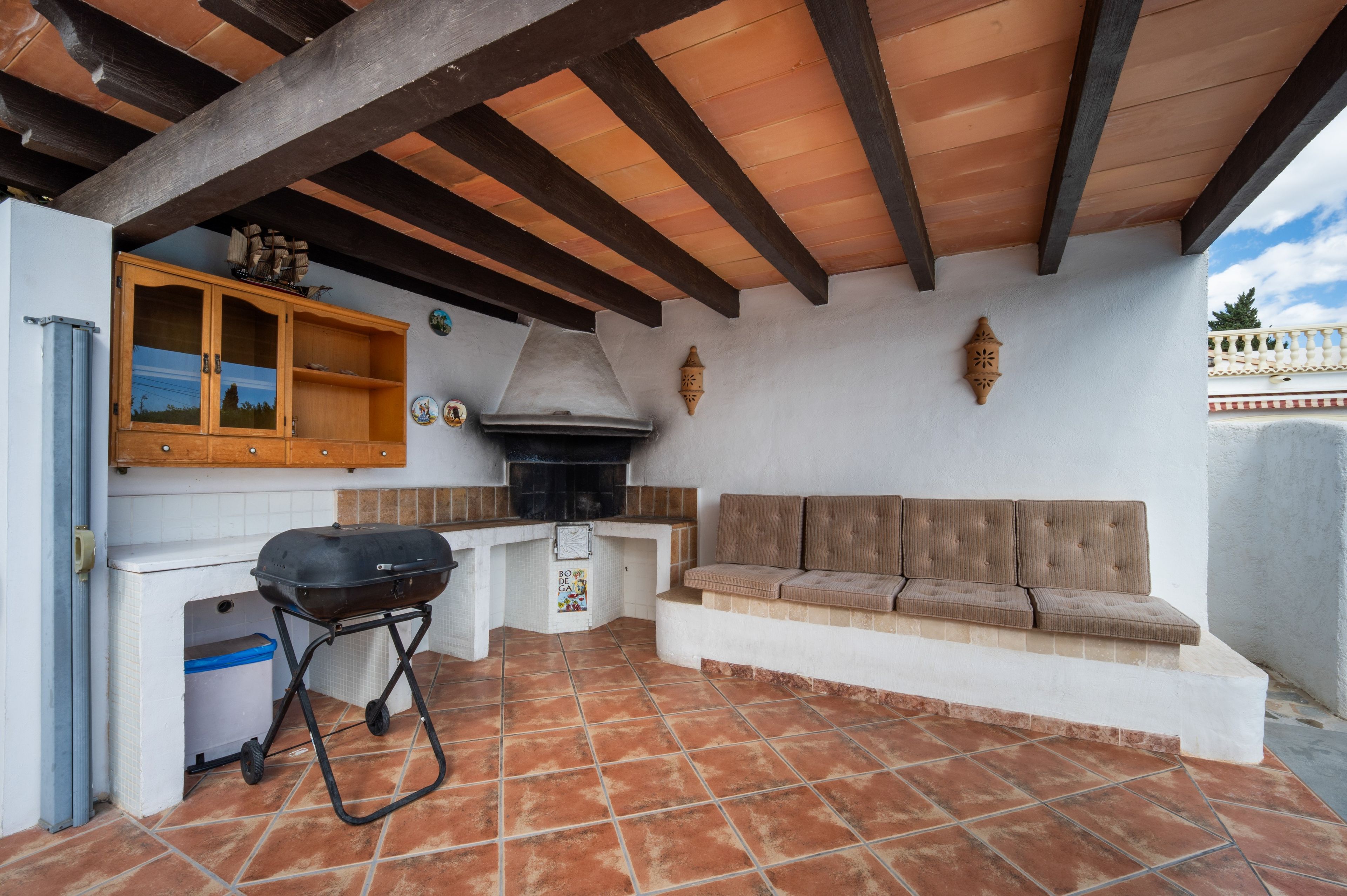 Un patio esterno con una griglia, un armadietto in legno e una zona salotto con cuscini.