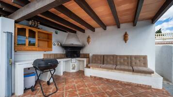 Un patio esterno con una griglia, un armadietto in legno e una zona salotto con cuscini.