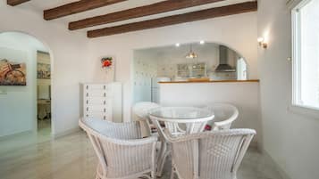 A dining area with wicker chairs, a glass-top table, and a kitchen in the background.