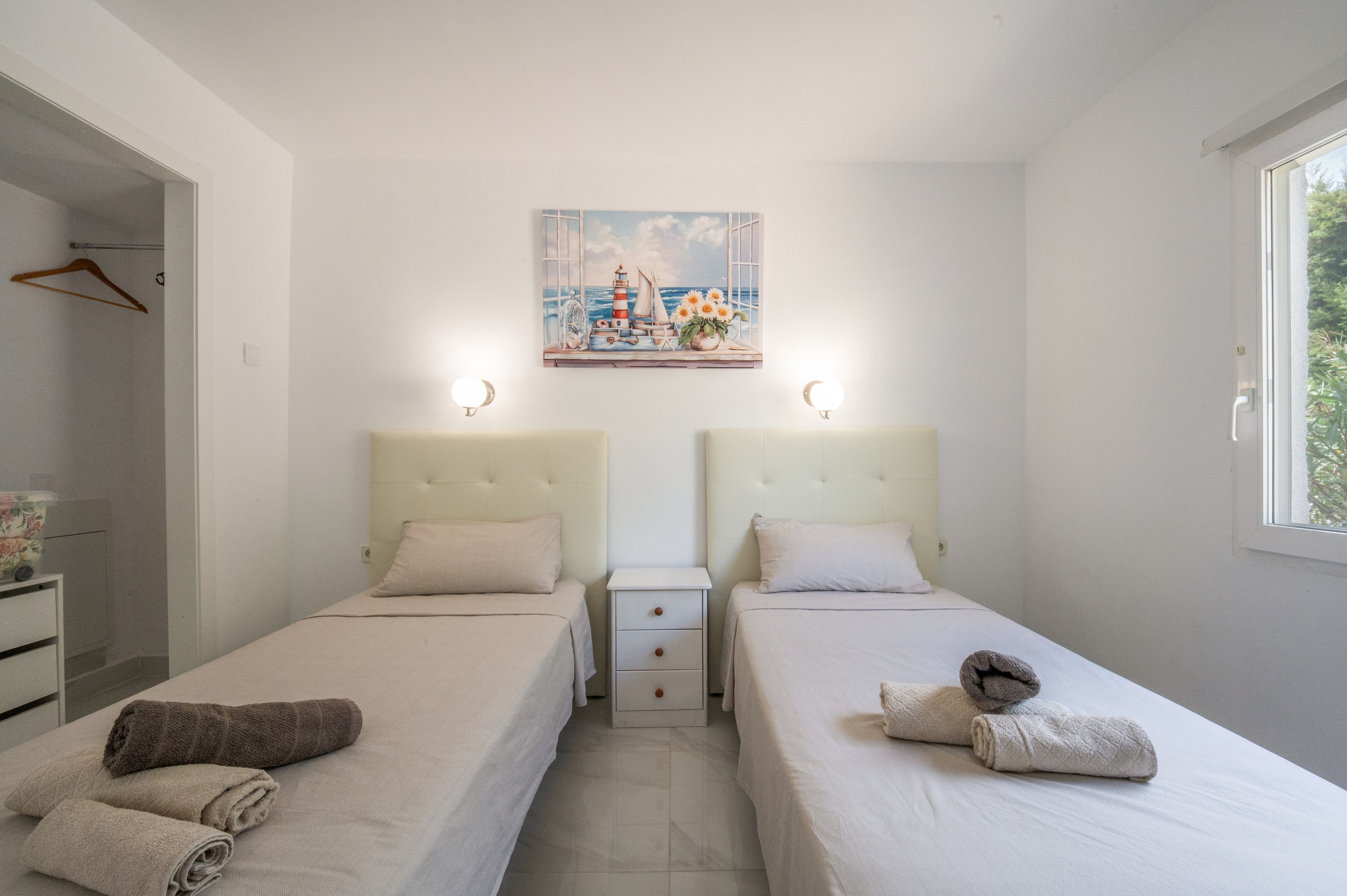 A twin bedroom with two beds, a nightstand, a dresser, a painting, and a window.