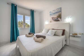 A bedroom with a bed, curtains, a painting, and a bedside table.