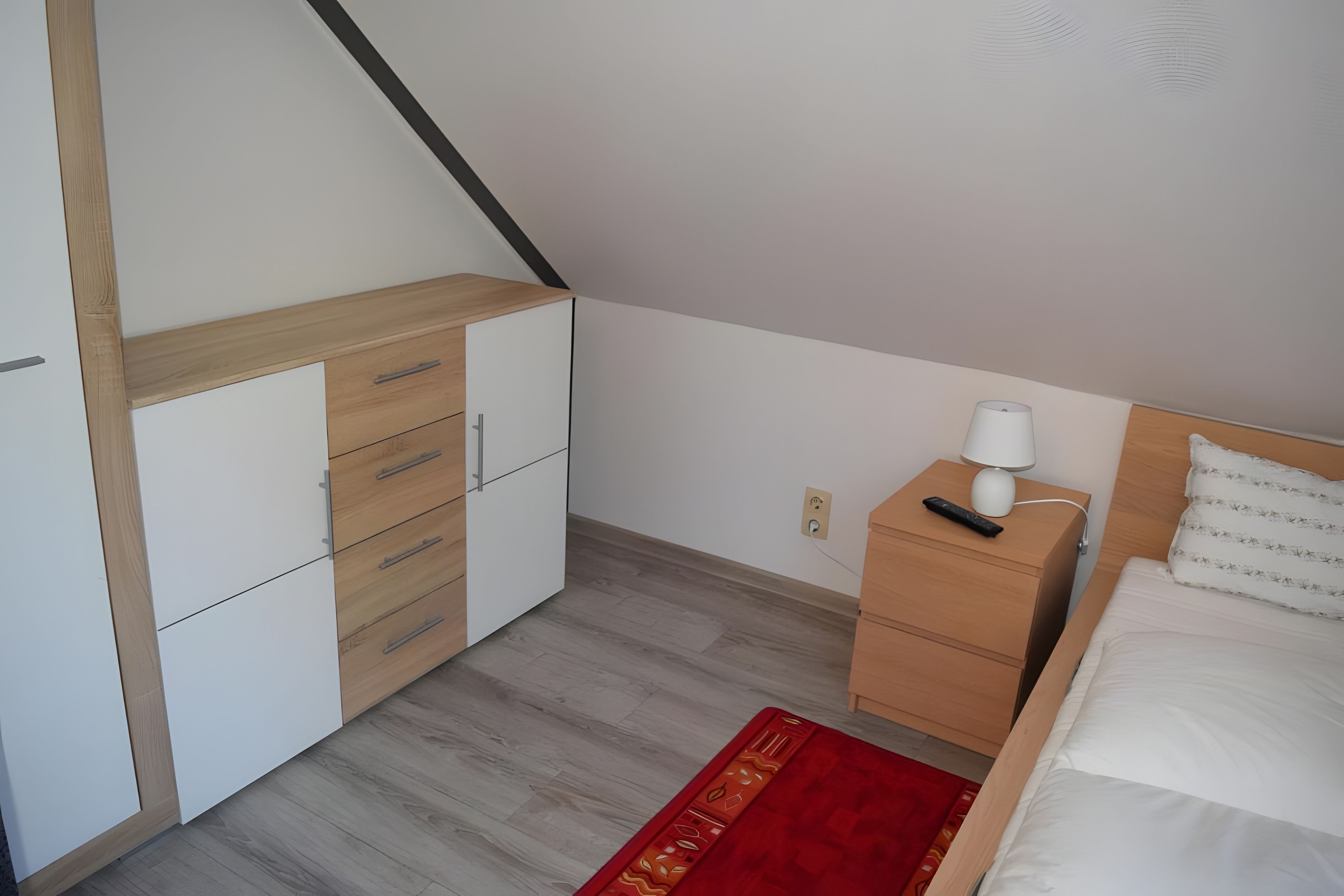 A bedroom with a bed, a nightstand, a dresser, and a red rug.