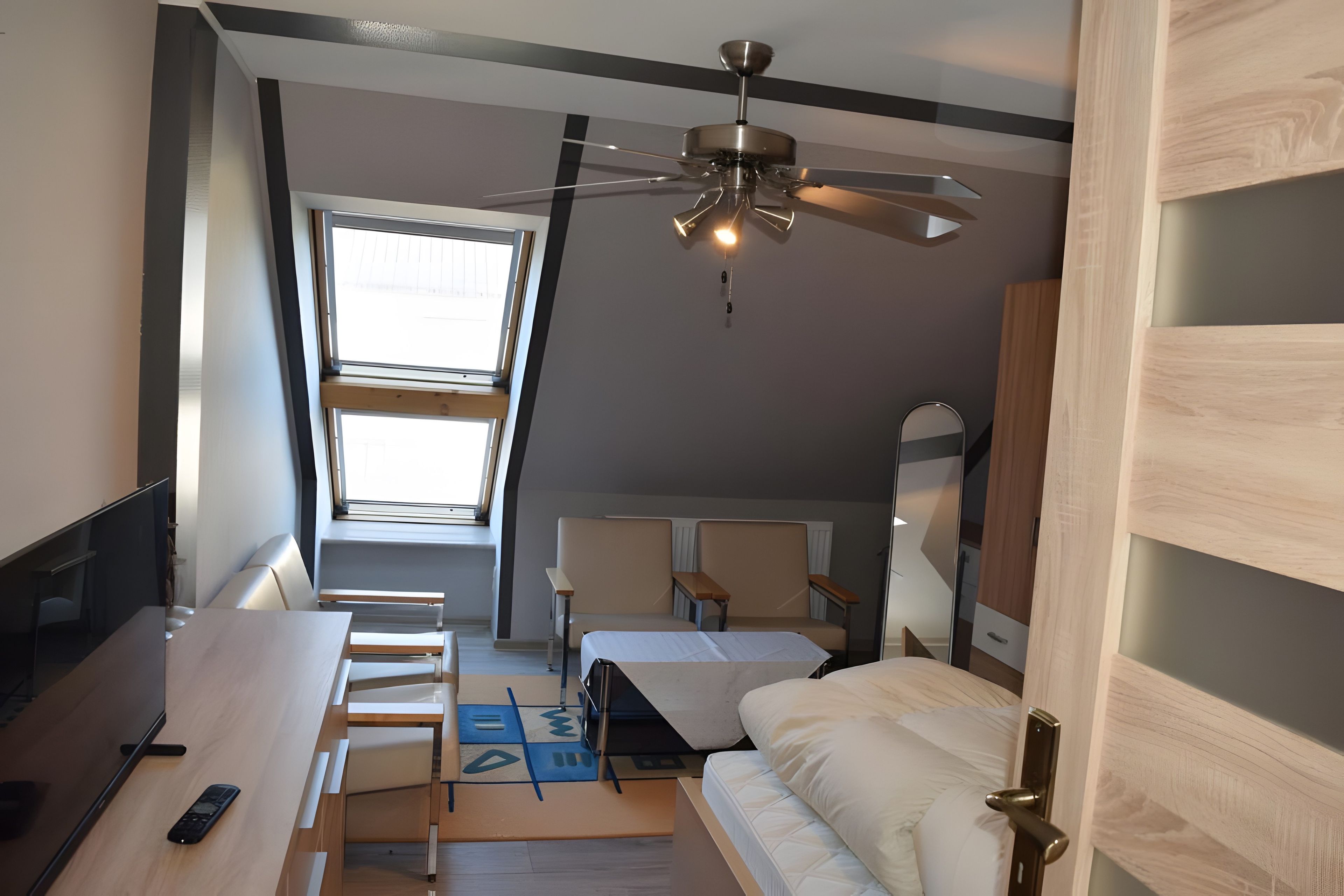 A compact room with a bed, a desk, a chair, and a ceiling fan.