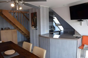 A modern kitchen with a built-in island, wooden staircase, and a dining area with a table and chairs.