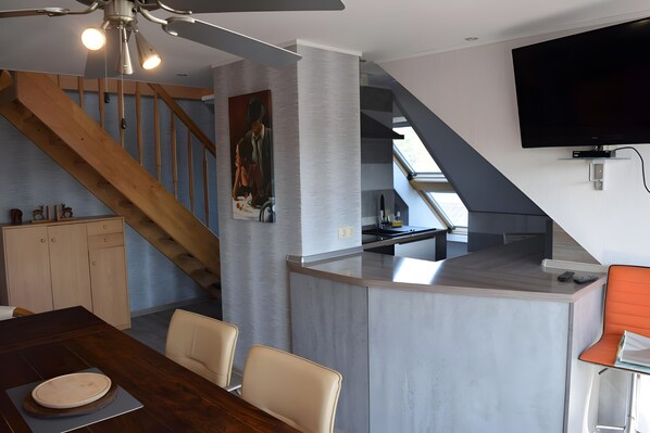 A modern kitchen with a built-in island, wooden staircase, and a dining area with a table and chairs.
