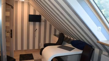 Une pièce dotée d’un plafond en pente, d’un téléviseur à écran plat fixé au mur, d’un bureau avec une chaise et d’une fenêtre donnant sur l’extérieur.