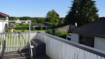 A residential balcony with a white railing, a grill, and a view of neighboring houses and trees.